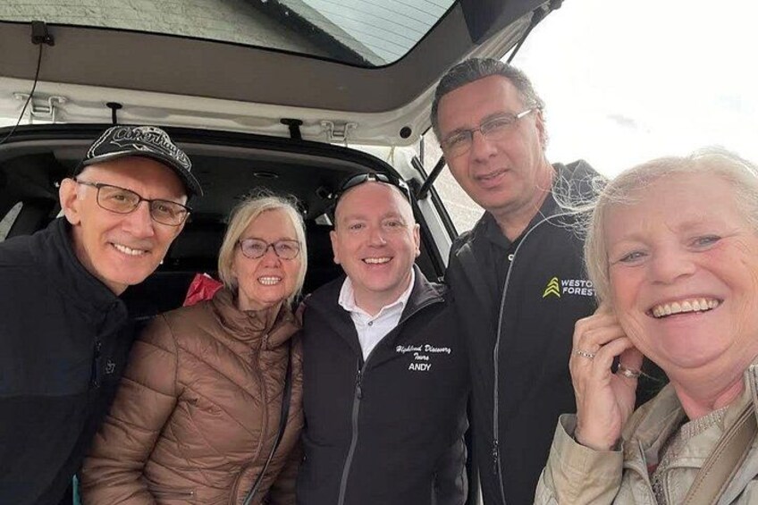 A group of people standing in a vehicle with open trunk. 3