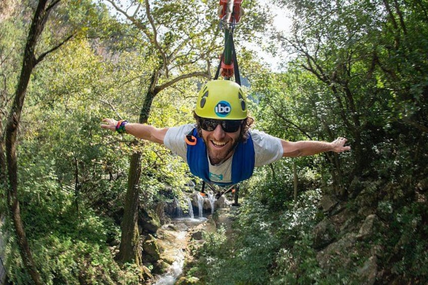 A person bungee jumping with a harness and helmet, surrounded by dense forest and a stream. 1