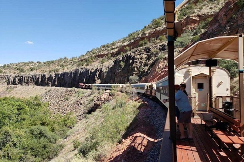 Un tren sobre una vía, un andén de madera y una ladera rocosa. 3