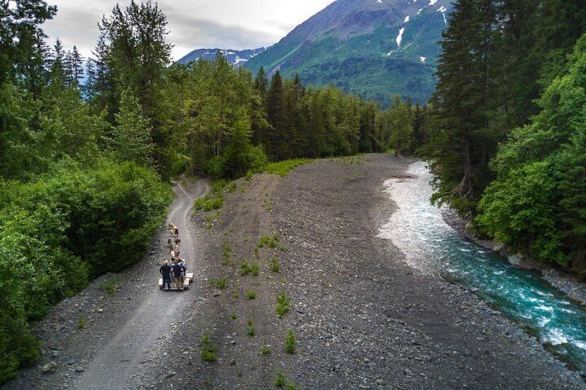 A group of people on a gravel road with a river on one side and a forest on the other. 2