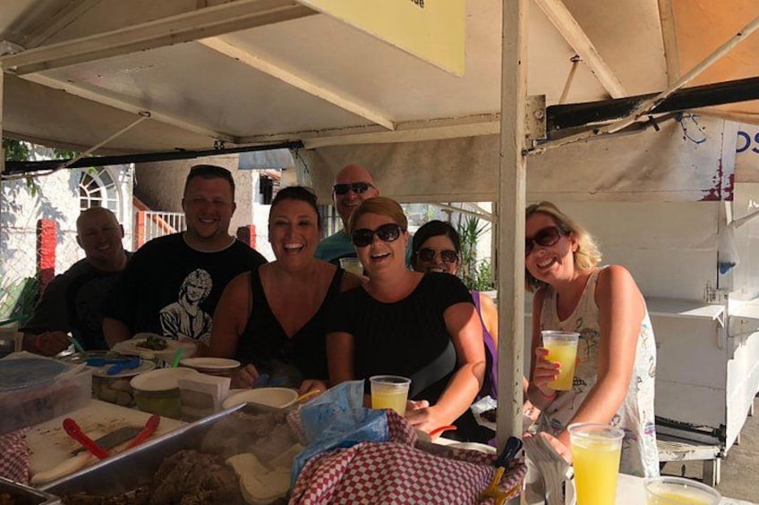 Un groupe de personnes est assis autour d’une table, où se trouvent de la nourriture et des boissons, et se trouve sous une tente. 2