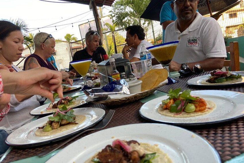 Des personnes dînent en plein air dans un restaurant, devant des assiettes remplies de nourriture et des boissons. 2