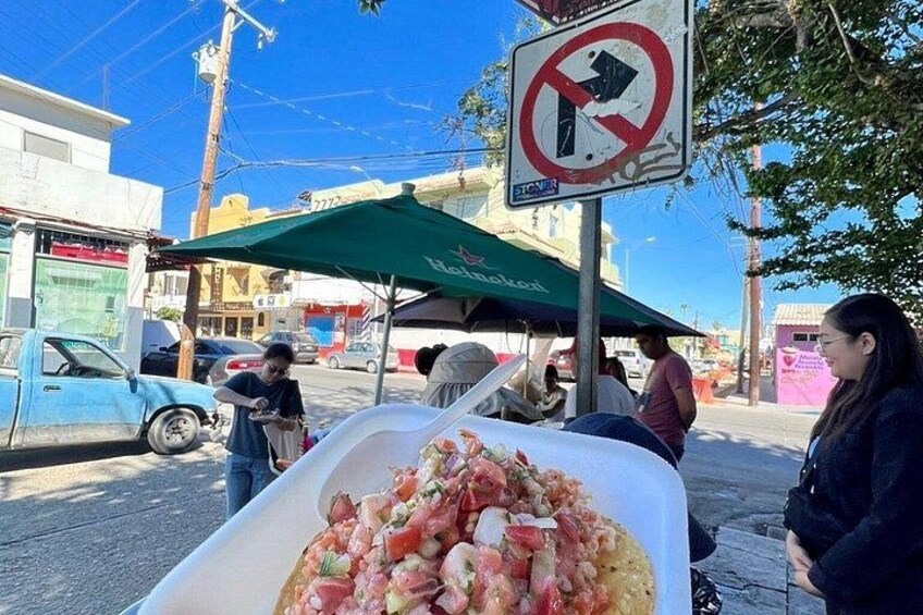 Een kraam met straatvoedsel, een grote bak met eten, een bord dat een rechtsafverbod aangeeft, en mensen die eromheen zitten. 2