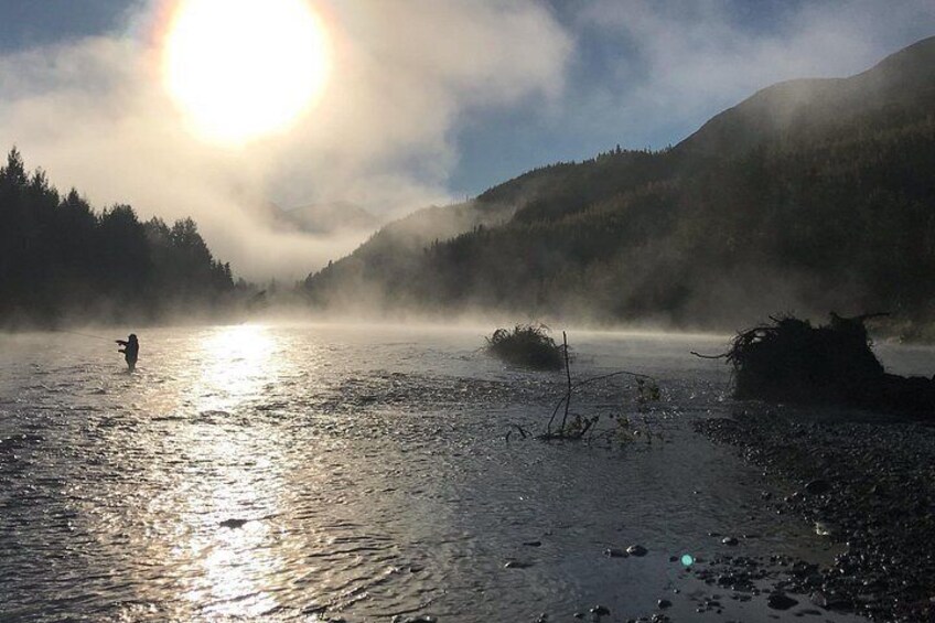 Ein nebliger See mit einem Angler, umgeben von Bergen und dichtem Wald. 2