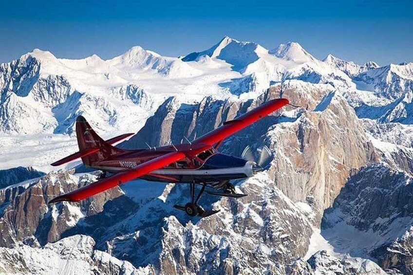 A red and white aircraft flying over snow-covered mountains. 3