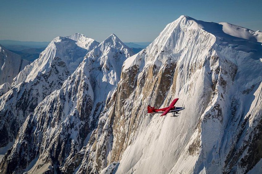 A red aircraft flying over snow-covered mountain peaks. 1
