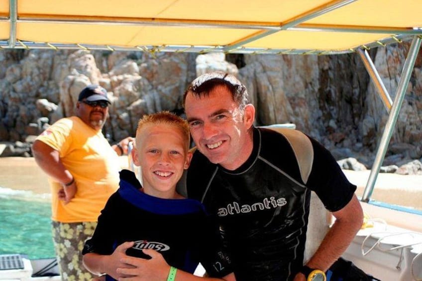 A person wearing a black vest with 'Atlantis' on it, standing near a rocky coastline. 5