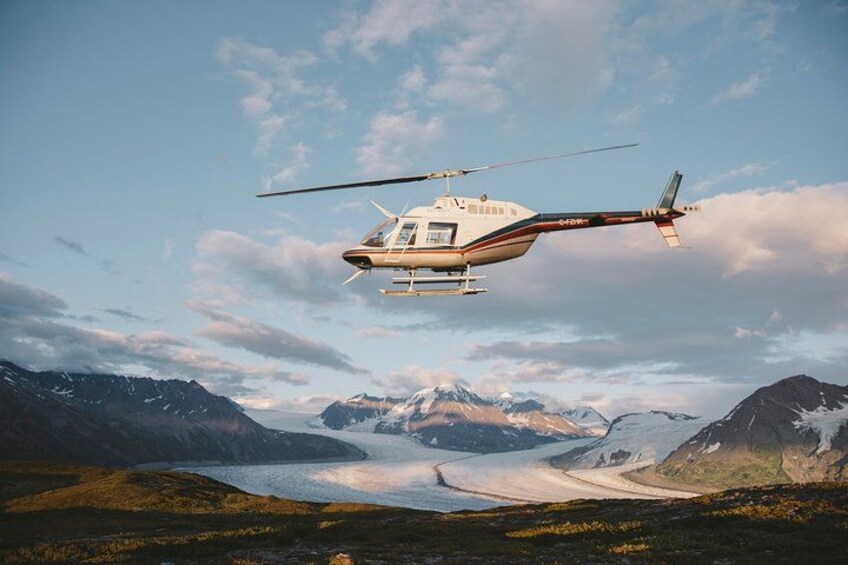 A helicopter flying over a mountainous landscape with a lake and snow-capped peaks in the background. 3