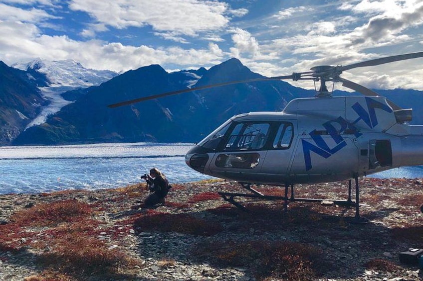 A helicopter with 'NPH' on its side parked near a body of water with mountains in the background. 5