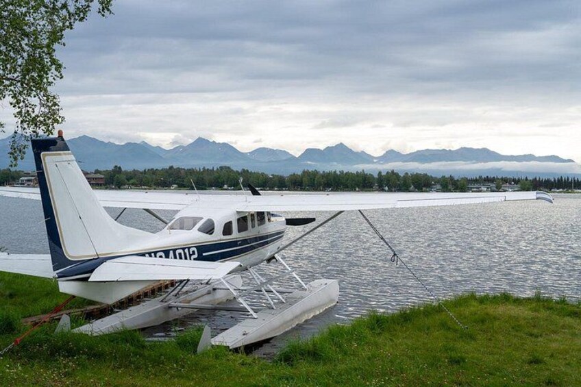 A seaplane parked on a grassy area near a body of water with mountains in the background. 2