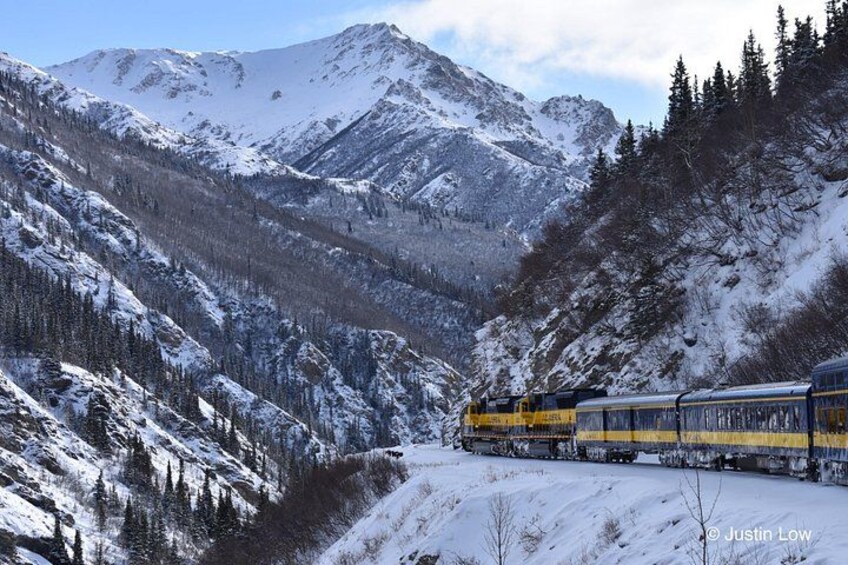 A train on a snowy mountain track surrounded by snow-covered trees and mountains. 2