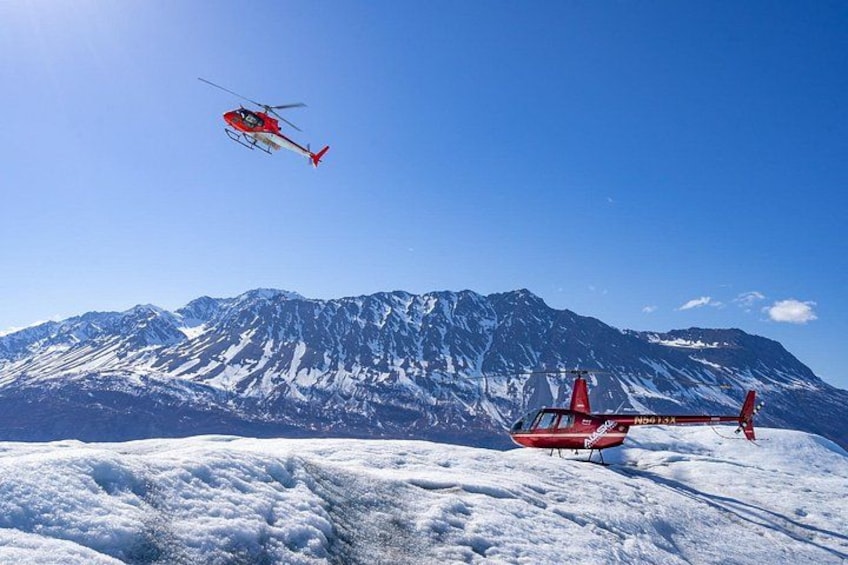 A red helicopter flying over a snowy mountain range. 3