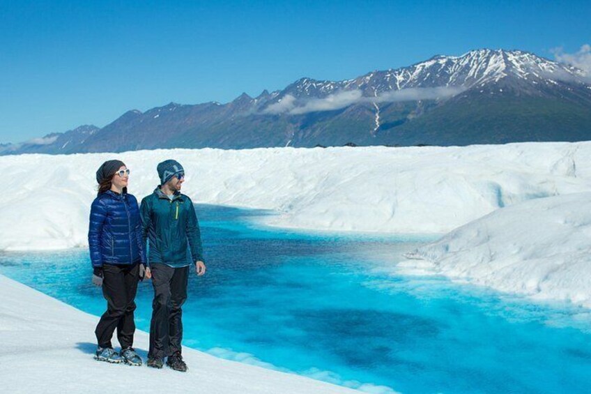 Two people standing on a glacier with a mountain range in the background. 5