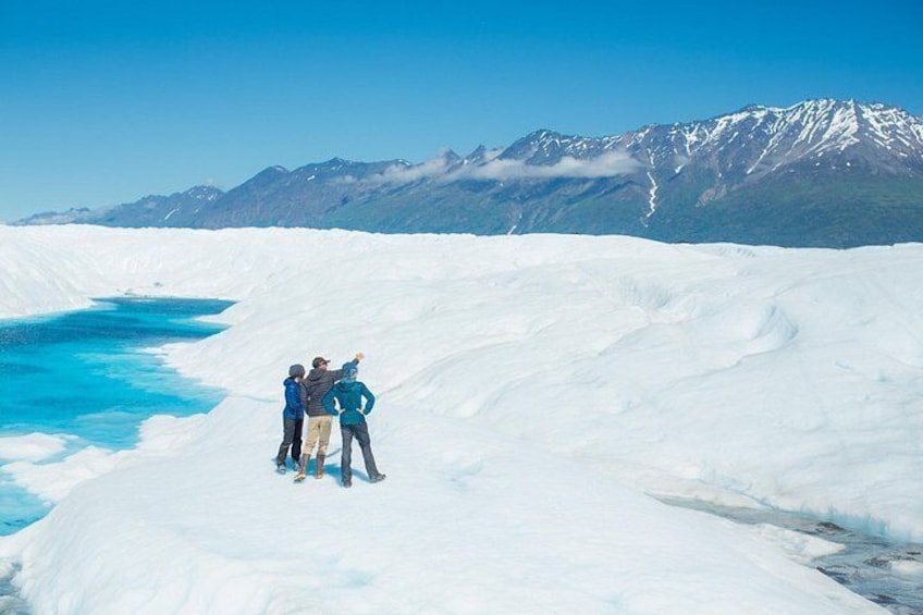 A glacier with a blue water body and snow-covered mountains in the background. 4