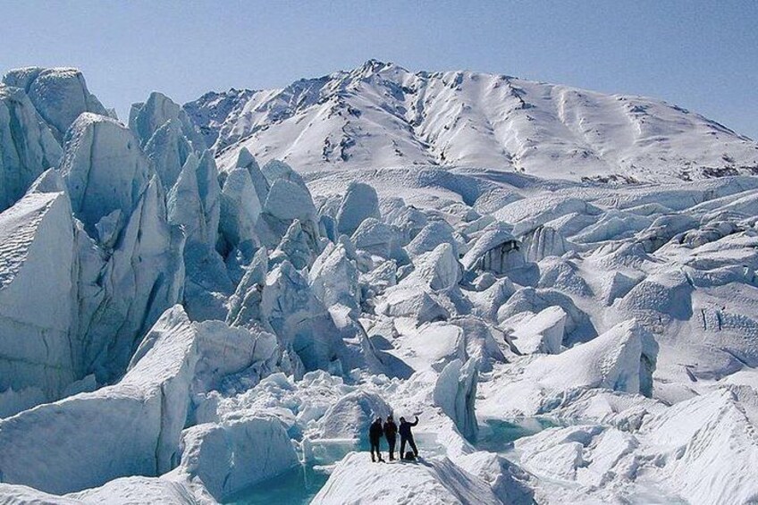 A glacier with ice formations and a group of people standing on the snow. 2