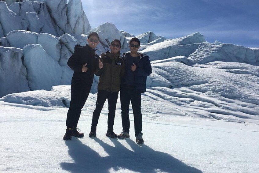 Three people standing on a snowy landscape with large ice formations in the background. 2
