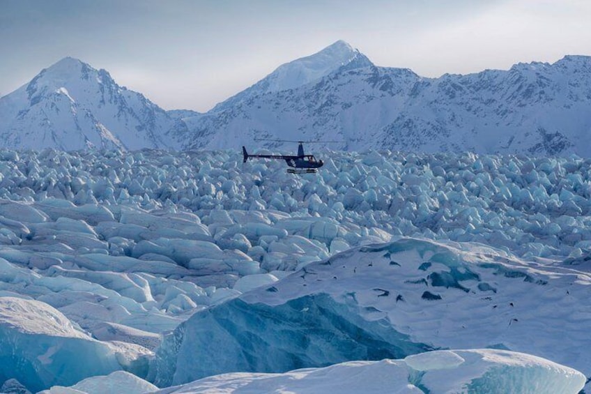 Un helicóptero sobrevolando una extensión inmensa de nieve y hielo, con montañas al fondo. 4