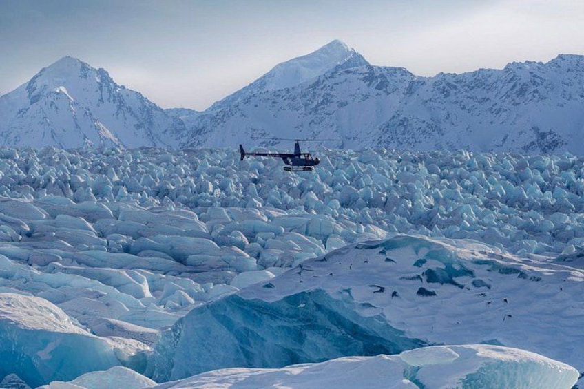 A helicopter flying over a vast expanse of snow and ice with mountains in the background. 4