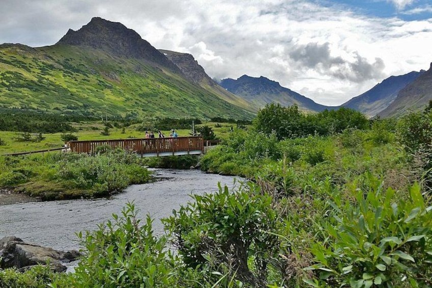 Un pont en bois enjambant une rivière, entouré d’une végétation luxuriante et de montagnes. 3