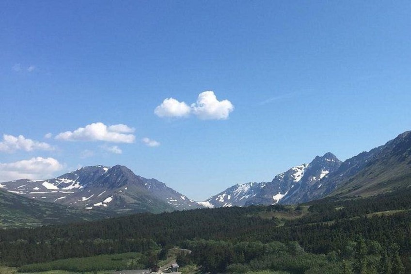 Un paysage montagneux avec des sommets enneigés, des forêts denses et un ciel bleu clair. 2