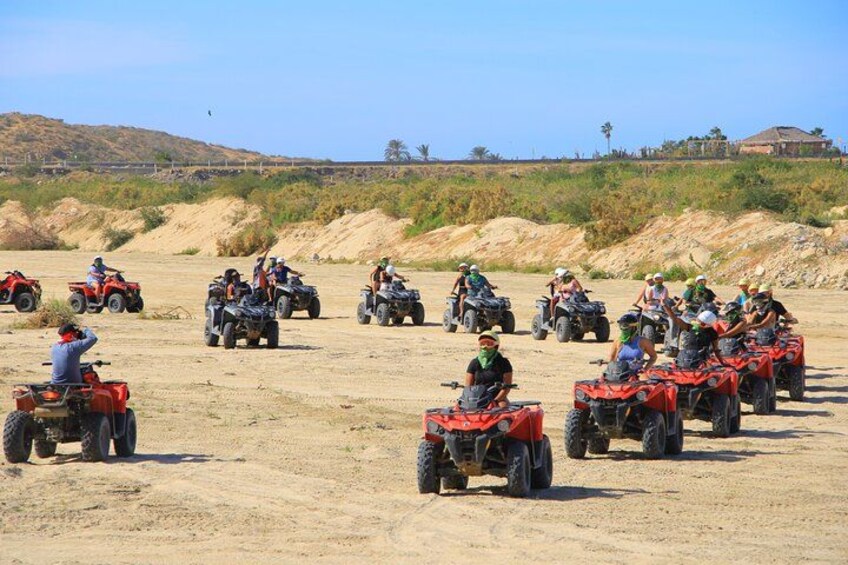 Un grupo de personas manejando cuatrimotos rojas por un sendero de tierra en un entorno desértico con poca vegetación y colinas al fondo. 1