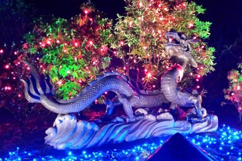 Una escultura de dragón con escamas iluminadas y un jinete, frente a un fondo de árboles y luces azules. 3