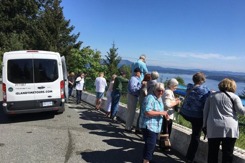 Un gruppo di persone in piedi lungo una strada, con un furgone con la scritta 'Island Time Tours' e uno scorcio panoramico di un lago e montagne sullo sfondo. 1