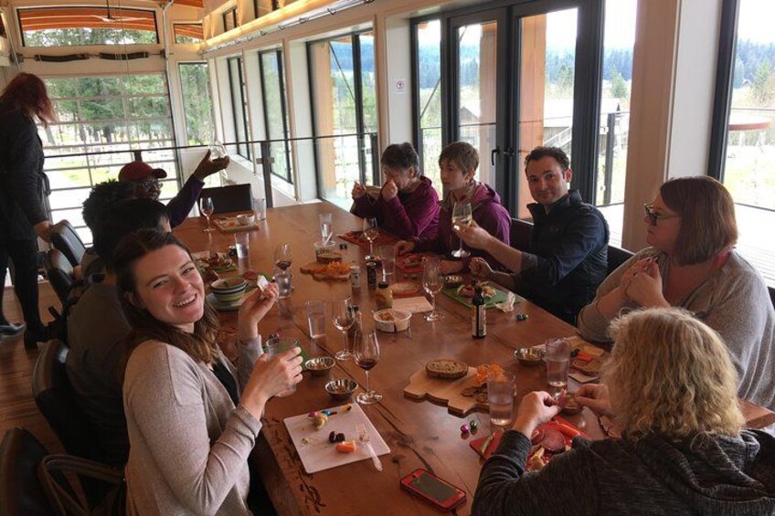 Un gruppo di persone sta cenando a un tavolo di legno, con calici di vino e piatti di cibo. 2