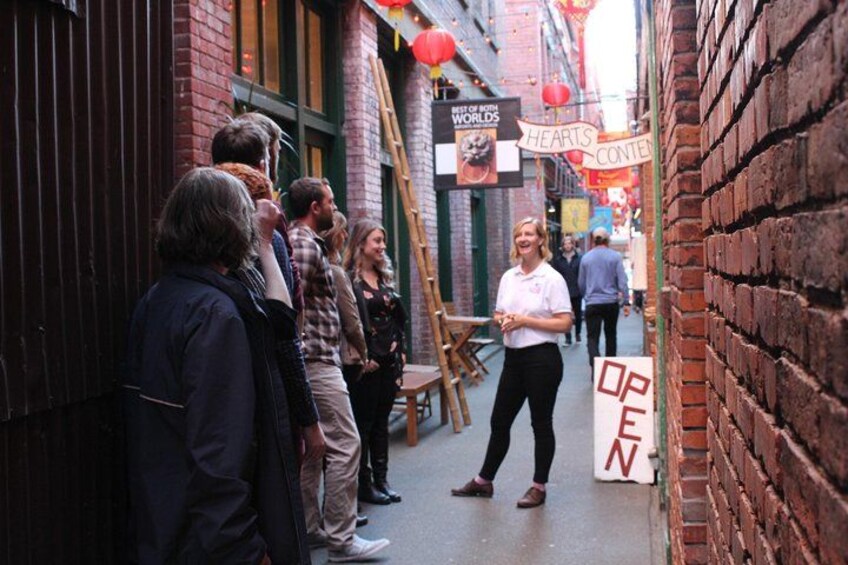A narrow alley with brick walls, a person standing with a sign that says "OPEN," and another sign that reads "HEARTS CONTENT." 2
