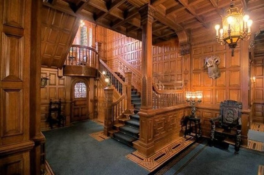 A grand wooden staircase with intricate carvings, a chandelier, and a large animal head mounted on the wall. 4