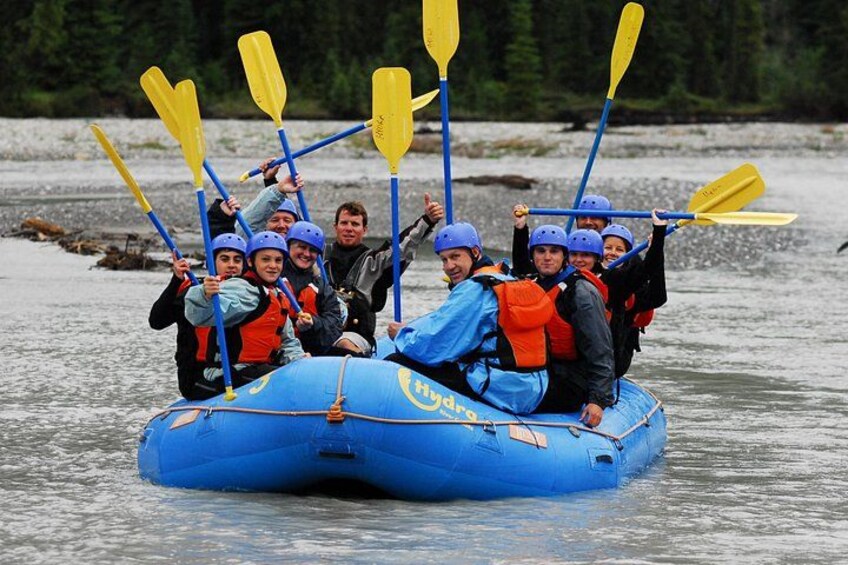 A group of people on a blue inflatable raft with paddles, wearing helmets and life jackets, on a river. 2