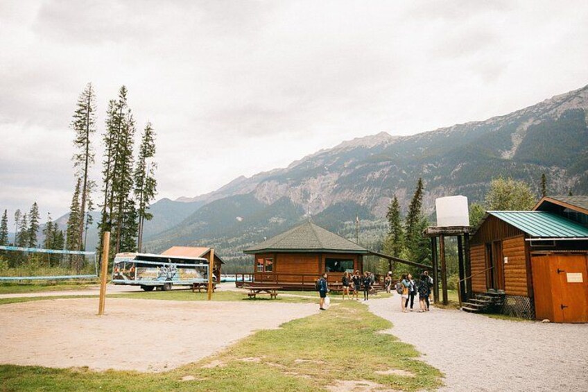 A wooden cabin with a green roof, a dirt path, and a mountainous backdrop. 4