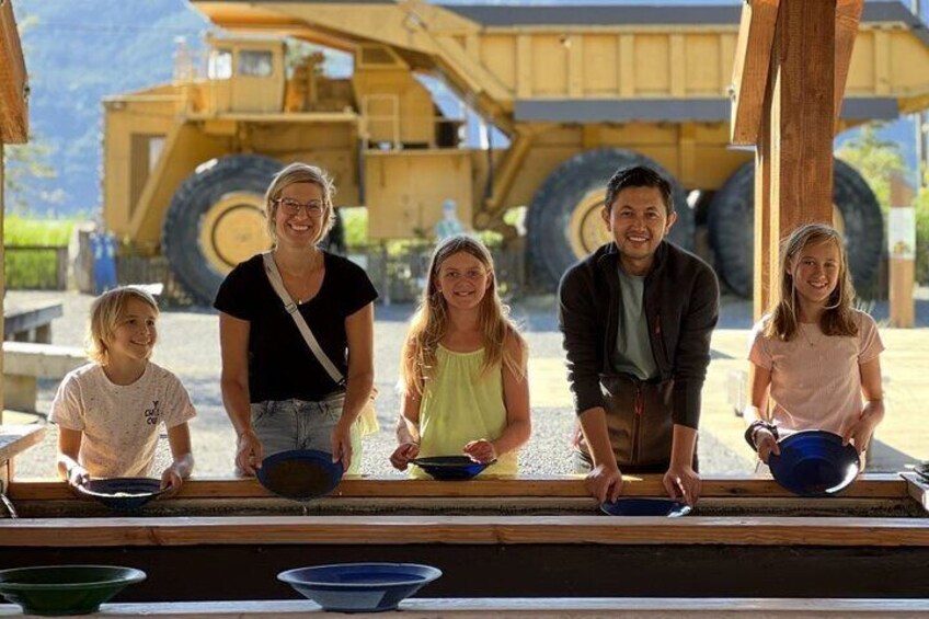 Una familia de cinco personas parada frente a un vehículo de construcción amarillo de gran tamaño. 4