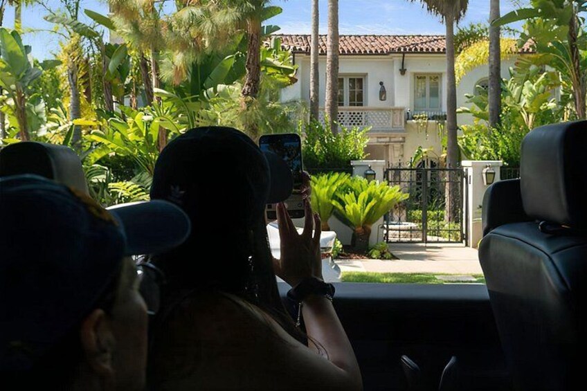 Iemand maakt een foto met een smartphone, het interieur van een auto, en een huis met een pannendak op de achtergrond. 2