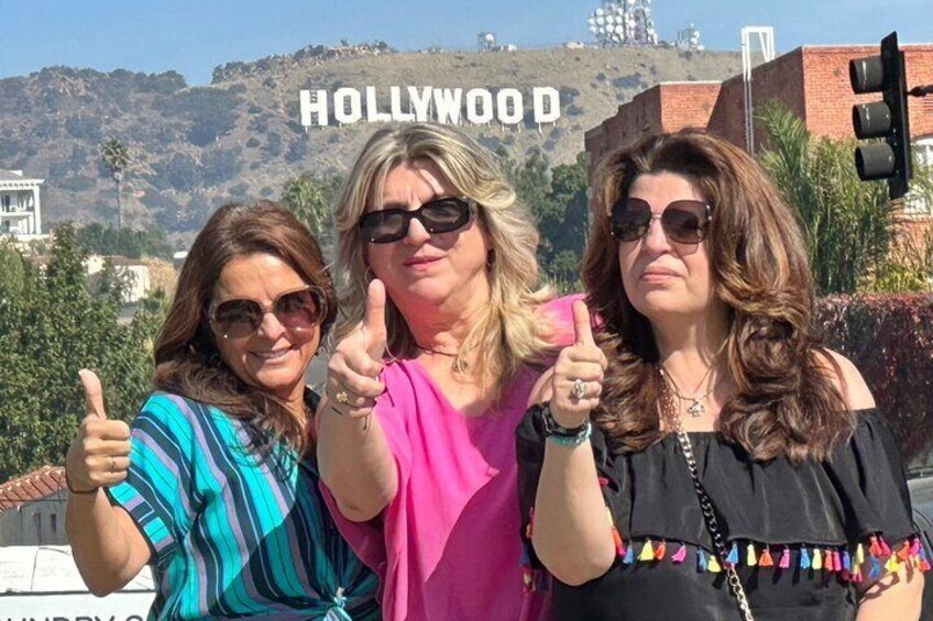 Three people giving thumbs up in front of the Hollywood sign. 1