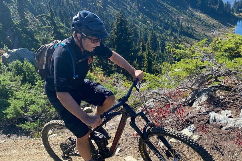 Eine Person fährt mit einem Mountainbike auf einem Pfad vor einer bewaldeten Bergkulisse. 2