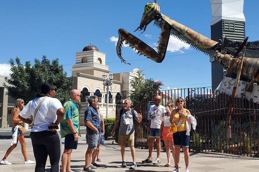A large mechanical dragon sculpture in an outdoor public space with people observing it. 5