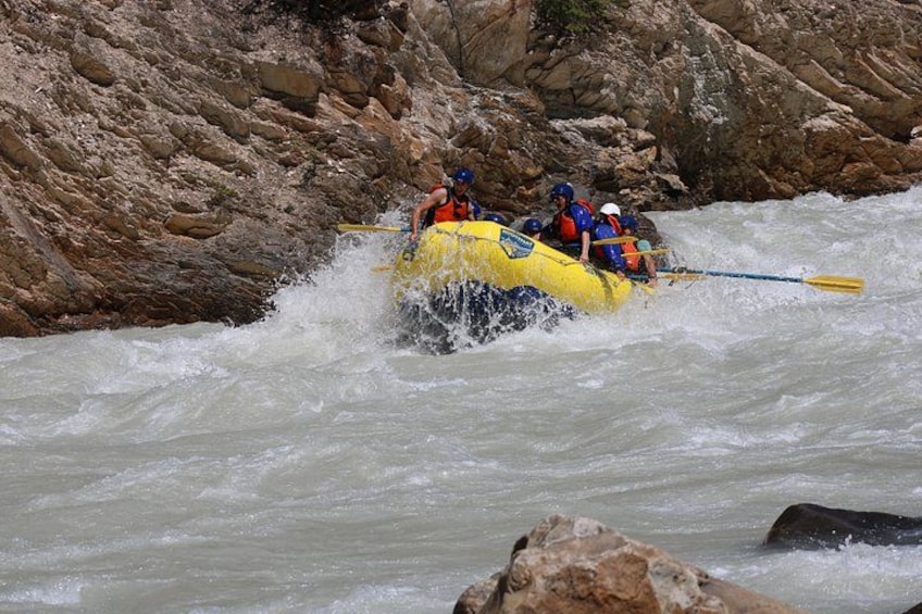 A group of people in a yellow raft navigating through a river with rapids, surrounded by rocky terrain. 4