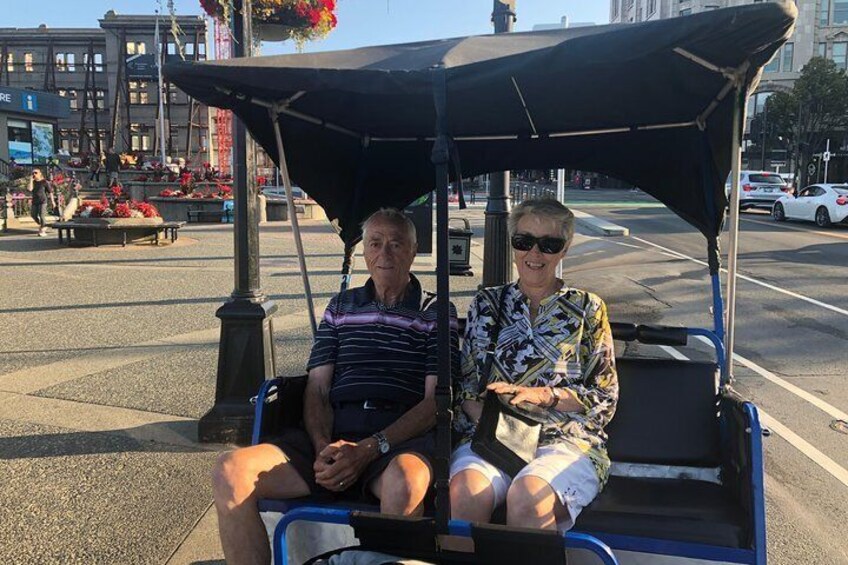 Two people seated in a covered cart on a city street. 3