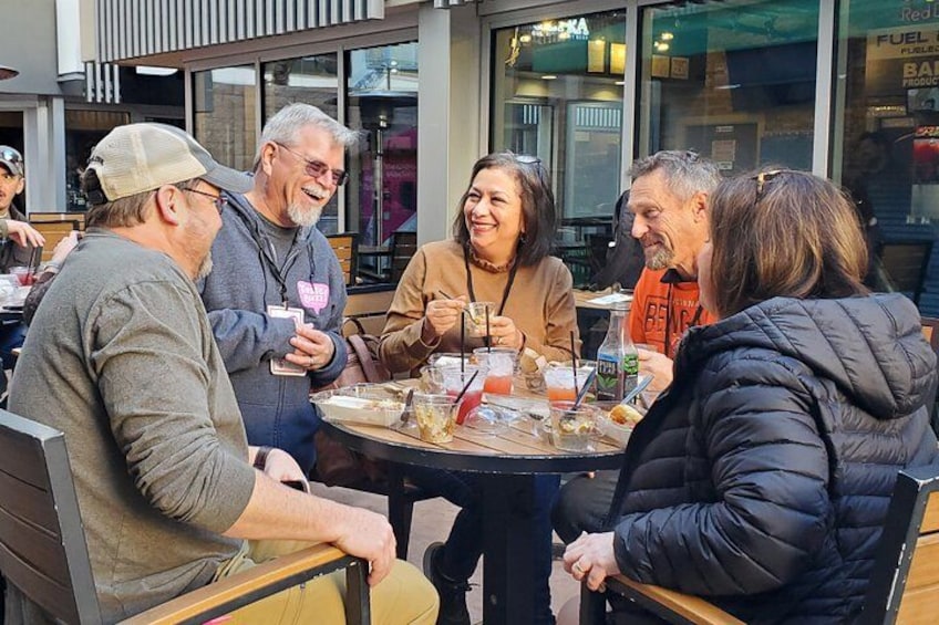 A group of people sitting around a table outdoors, engaged in conversation. 2
