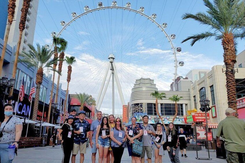 A group of people standing in front of a Ferris wheel with palm trees and buildings in the background. 2