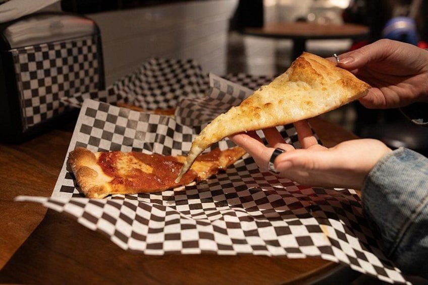 A person holding a slice of pizza on a checkered paper. 1