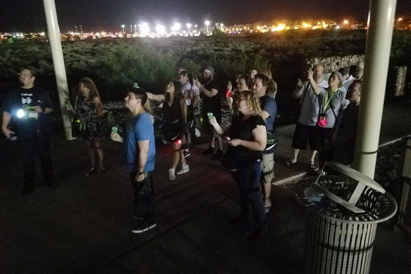 Een groep mensen die 's nachts buiten staan, waarvan sommigen lichtgevende apparaten vasthouden. 4