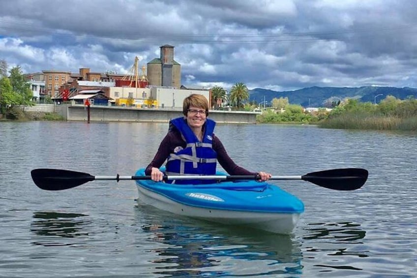 A person kayaking on a body of water with buildings and mountains in the background. 3