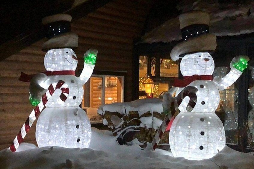Two illuminated snowmen with candy cane arms and a log cabin in the background. 3
