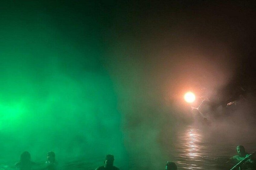 A nighttime scene with a green light and a bright light source reflecting on water. 2