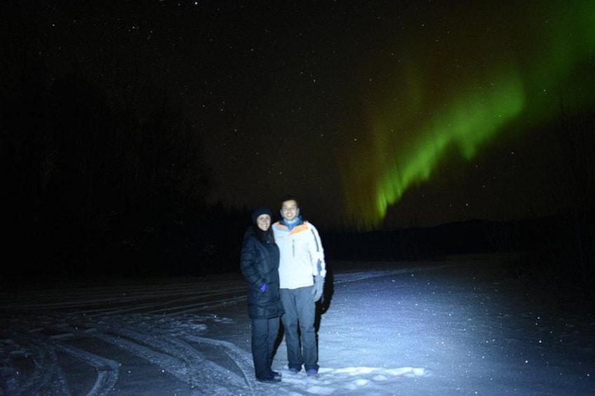 Two people standing on a snowy road under a night sky with the aurora borealis. 3