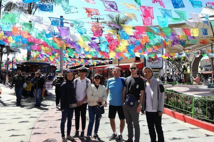 Un grupo de personas de pie en una plaza con decoraciones de papel de colores colgando. 2