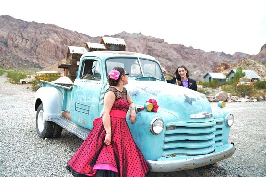 Una camioneta azul antigua con una mujer de vestido rojo a su lado. 4