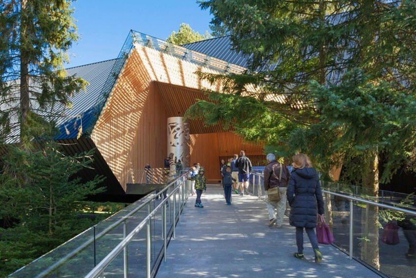 A modern building with a sloped roof and a glass walkway leading to it. 2